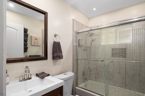 Une salle de bain avec un lavabo blanc, un miroir, une douche en verre et des toilettes.