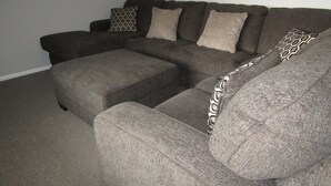 A sectional sofa with a matching ottoman in a living room with plain walls and a carpeted floor. - Reel Em Inn - Esplanade position.  Winter off peak special! (Point Turton)