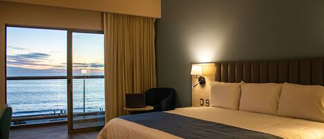 Habitación de hotel con una cama grande, un escritorio, una silla y vistas al mar.