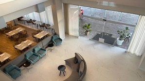 Eine großzügige Lobby mit einer gebogenen, grauen Couch, türkisfarbenen Ohrensesseln und einem Essbereich mit Tischen und Stühlen.