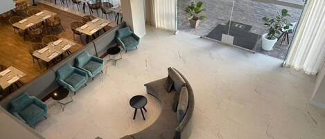 A spacious lobby with a curved gray sofa, teal armchairs, and a dining area with tables and chairs.