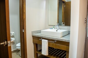 Un baño con tocador de madera, un lavabo blanco y un espejo.