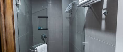 Un baño moderno con baldosas grises, cabina de ducha de vidrio, toallero y un pequeño estante con artículos de aseo.