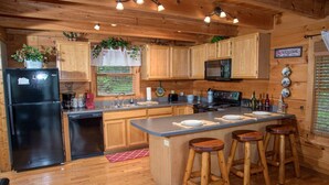 A wooden cabin kitchen with a refrigerator, stove, sink, and bar stools. - mountain view log cabin in Gatlinburg (Gatlinburg)