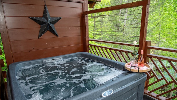 A hot tub with a star decoration, surrounded by a wooden deck and a railing, with a forest view. - mountain view log cabin in Gatlinburg (Gatlinburg)