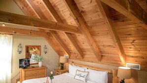 A cozy bedroom with a wooden ceiling, a bed with a 'BE OUR GUEST' pillow, bedside tables with lamps, and a small plant on the nightstand. - mountain view log cabin in Gatlinburg (Gatlinburg)