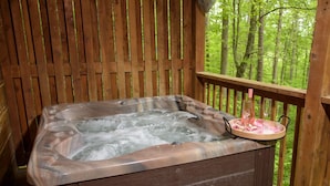A hot tub on a wooden deck with a wooden railing, surrounded by trees. - Cuddley Bears hideaway (Sevierville)