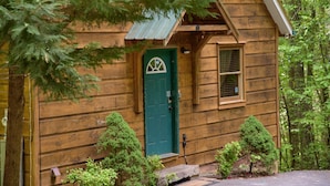 A wooden cabin with a green door, a small window, and a porch area with a bench. - Cuddley Bears hideaway (Sevierville)