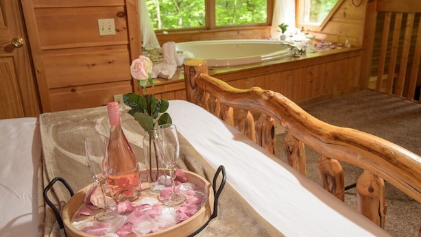 A wooden bed with a headboard, a bedside table with a tray holding a rose, a bottle, and glasses. - Cuddley Bears hideaway (Sevierville)