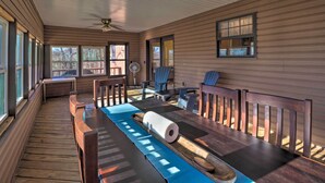 Um deck de madeira com mesa, cadeiras, ventilador de teto e janelas.