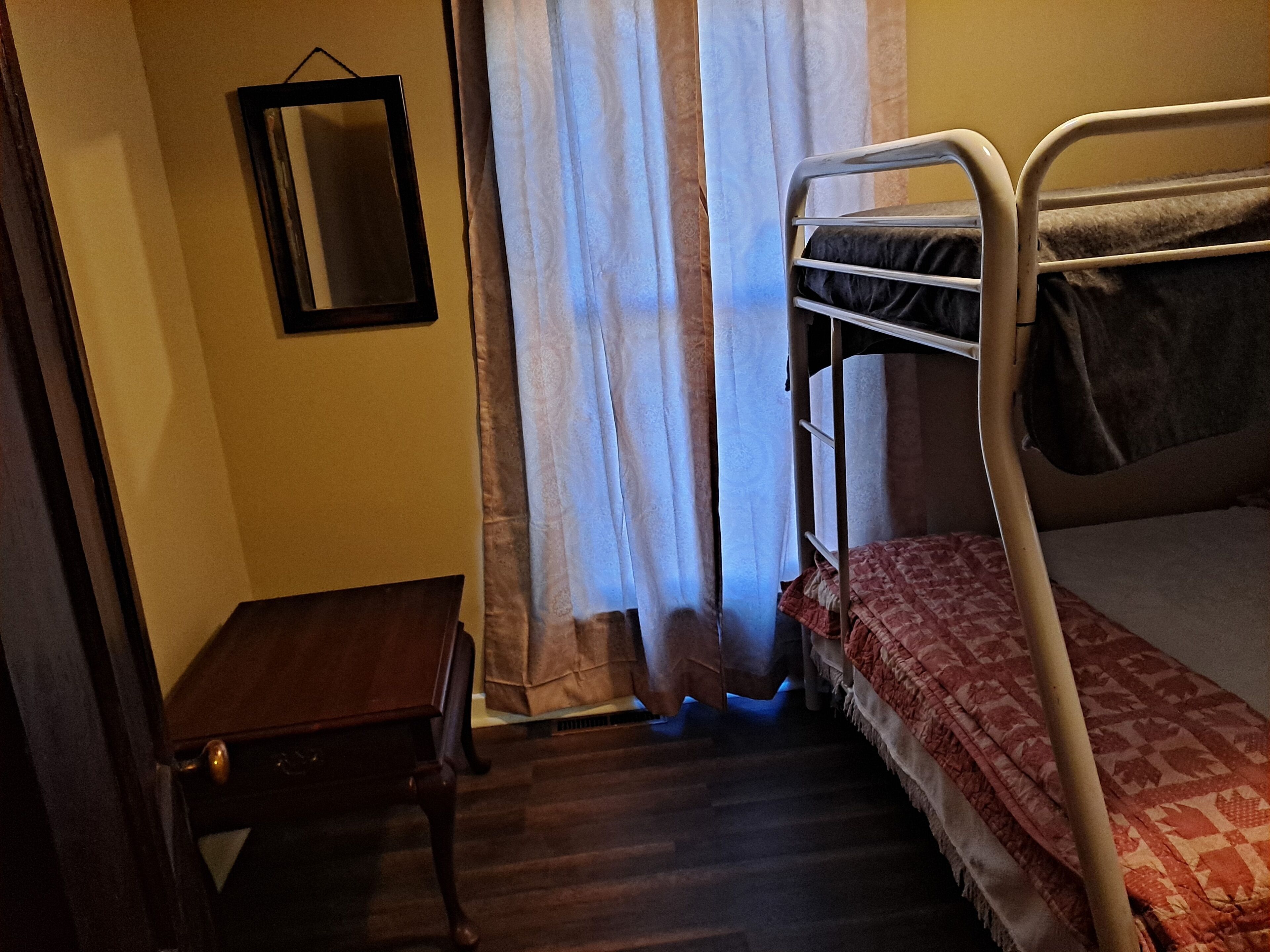 Una habitación pequeña y tenuemente iluminada con una cama litera, una mesita de madera y un espejo en la pared.