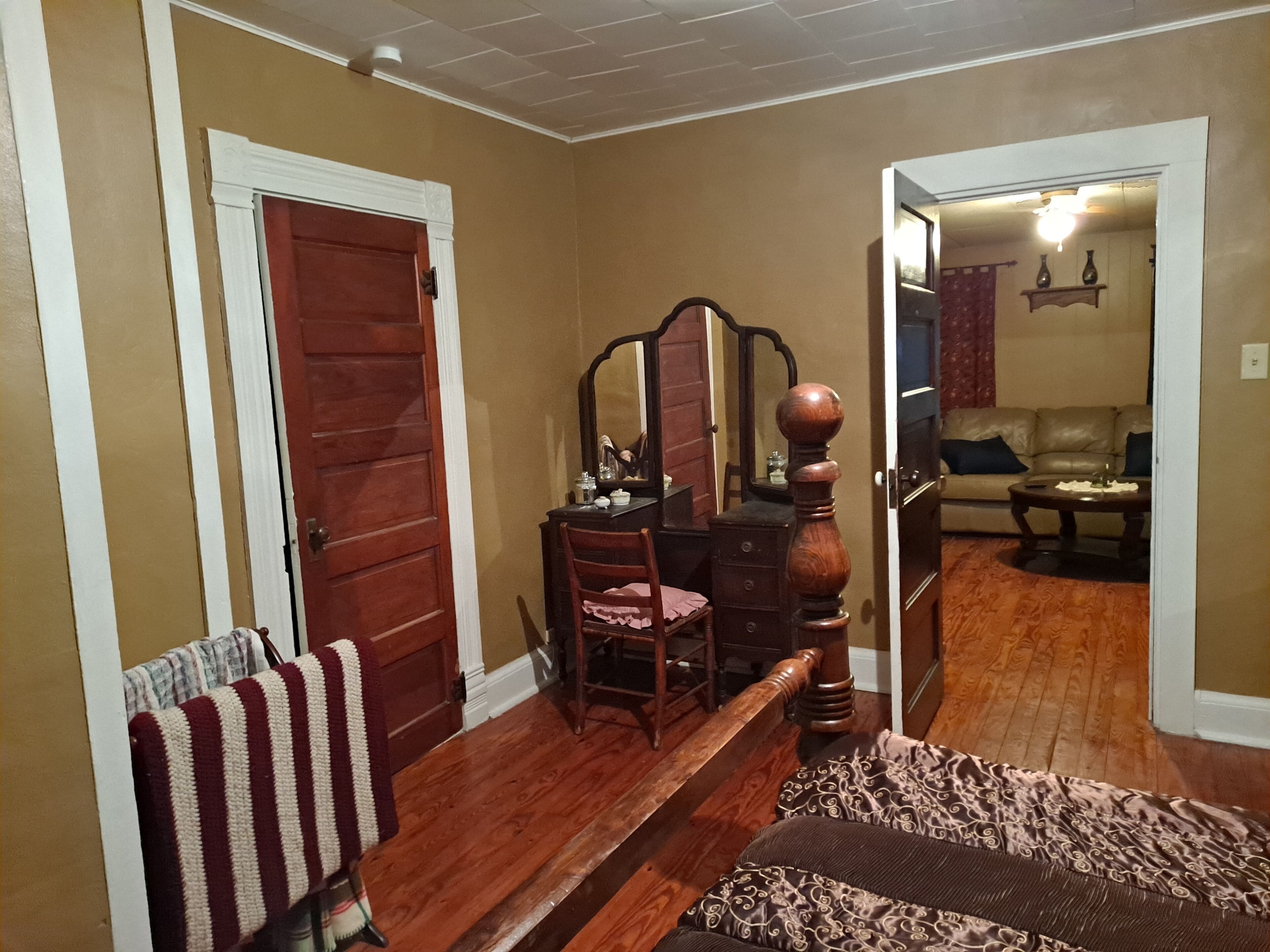 A room with a wooden bench, a chair, a dresser with a mirror, and a sofa in the background.