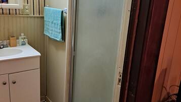 Ein Badezimmer mit einem weißen Waschbecken, einem Spiegel, einem Handtuchhalter mit einem blauen Handtuch und einer Duschkabinentür aus Glas.