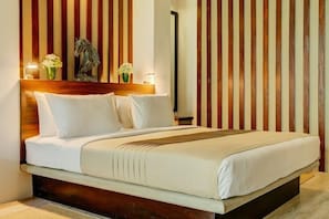 A neatly made bed with white linens and a wooden headboard, flanked by two vases of white flowers and a statue of a horse. - Lake Lodge (Colombo)