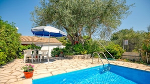 A swimming pool with a stone deck, a covered seating area, and a tree with a red decoration. - Fishermans Cottage: Private pool, a/c, near beach (Avlaki)