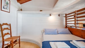 A bedroom with a bed, a wooden chair, a blue bedspread, and a white wall with a picture frame. - Fishermans Cottage: Private pool, a/c, near beach (Avlaki)