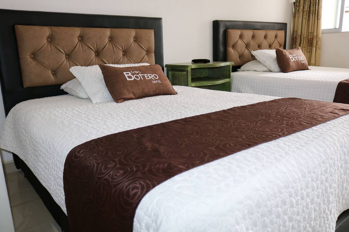Two twin beds with tufted headboards, a green nightstand, and a white textured bedspread.