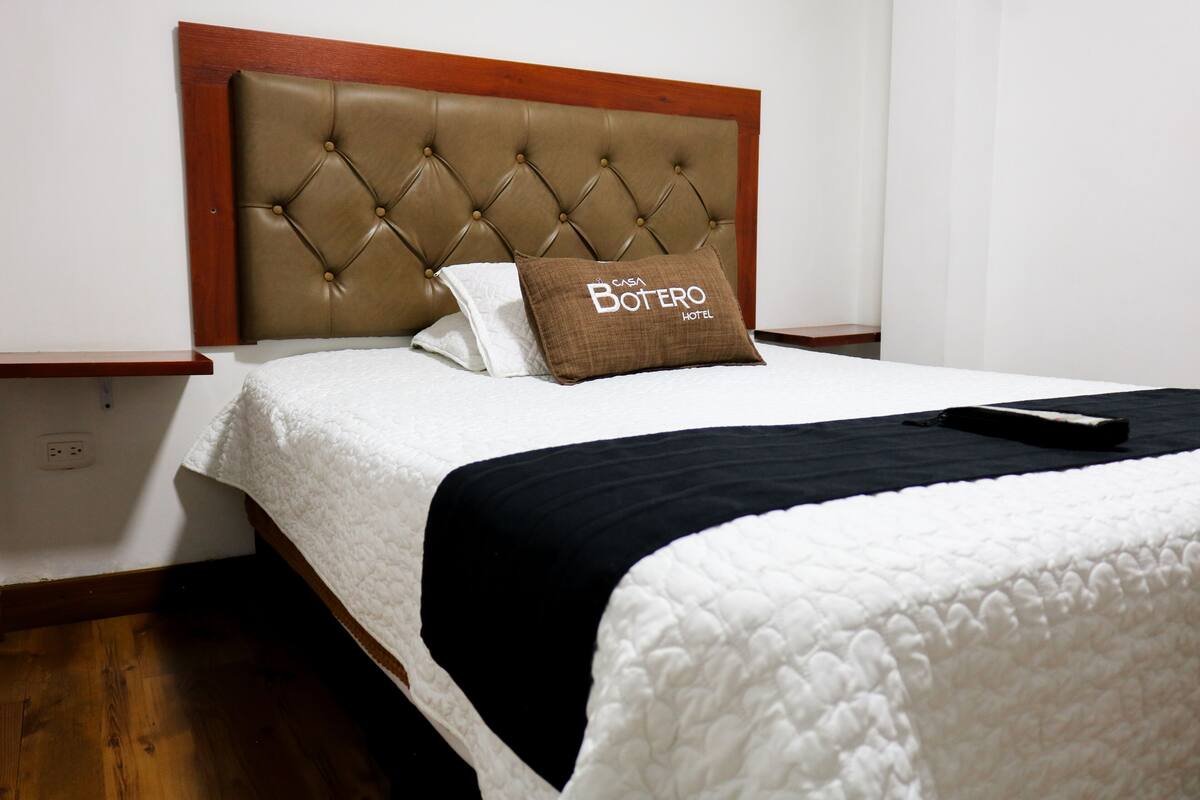 A neatly made bed with a tufted headboard, a pillow with text, and a remote control on the bed.