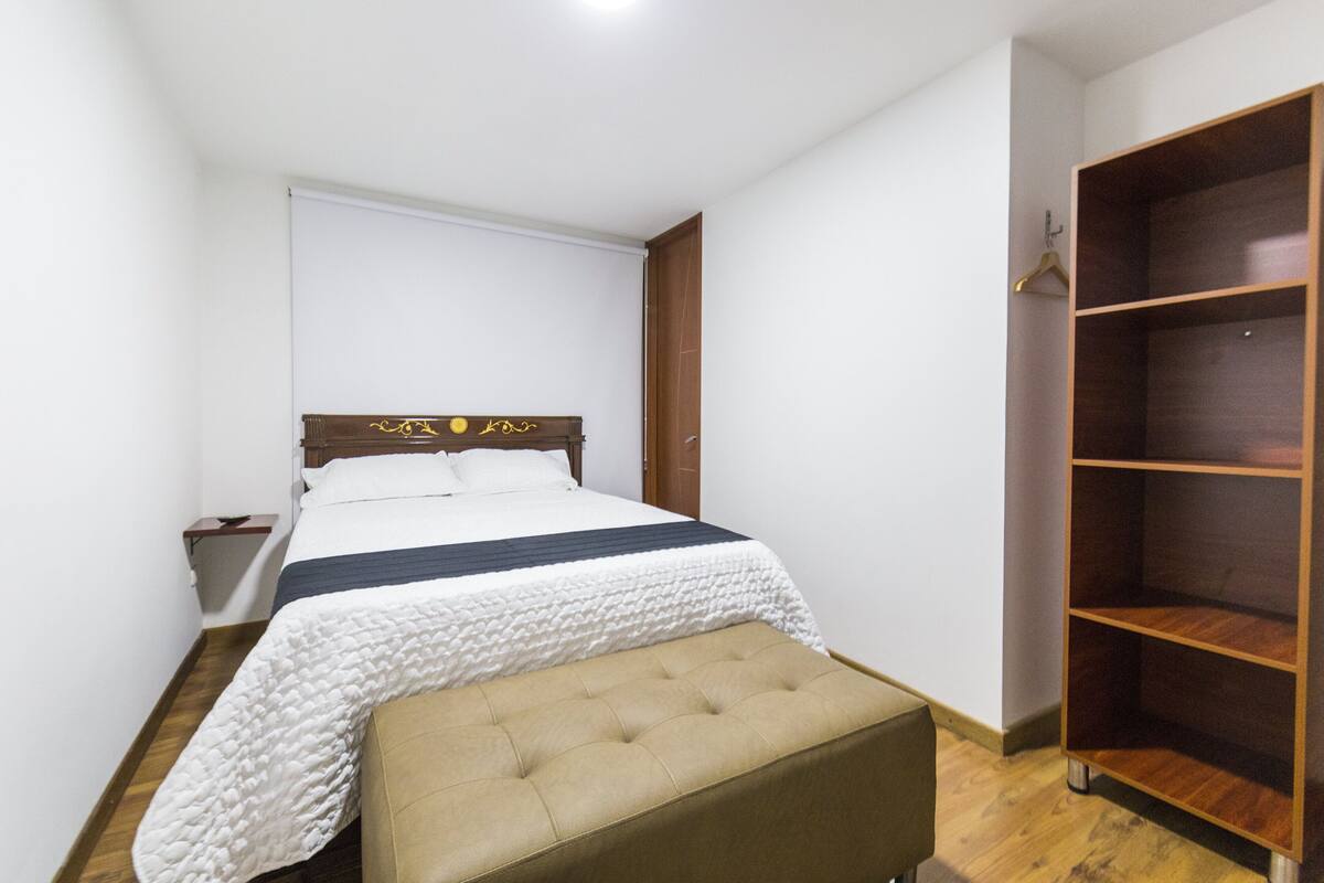 A bedroom with a bed, a bedside table, a wooden wardrobe, and a bench.