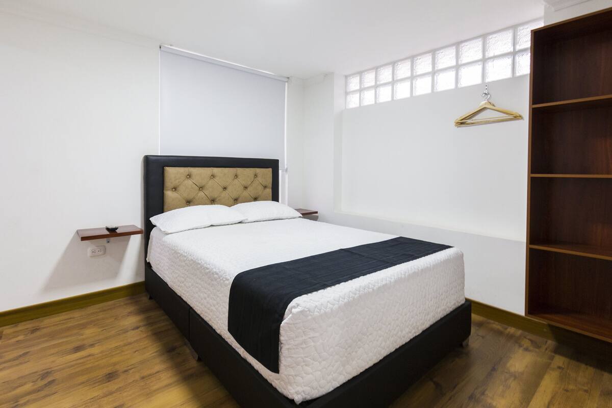 A bedroom with a bed, a wardrobe, a bedside table, and a window.
