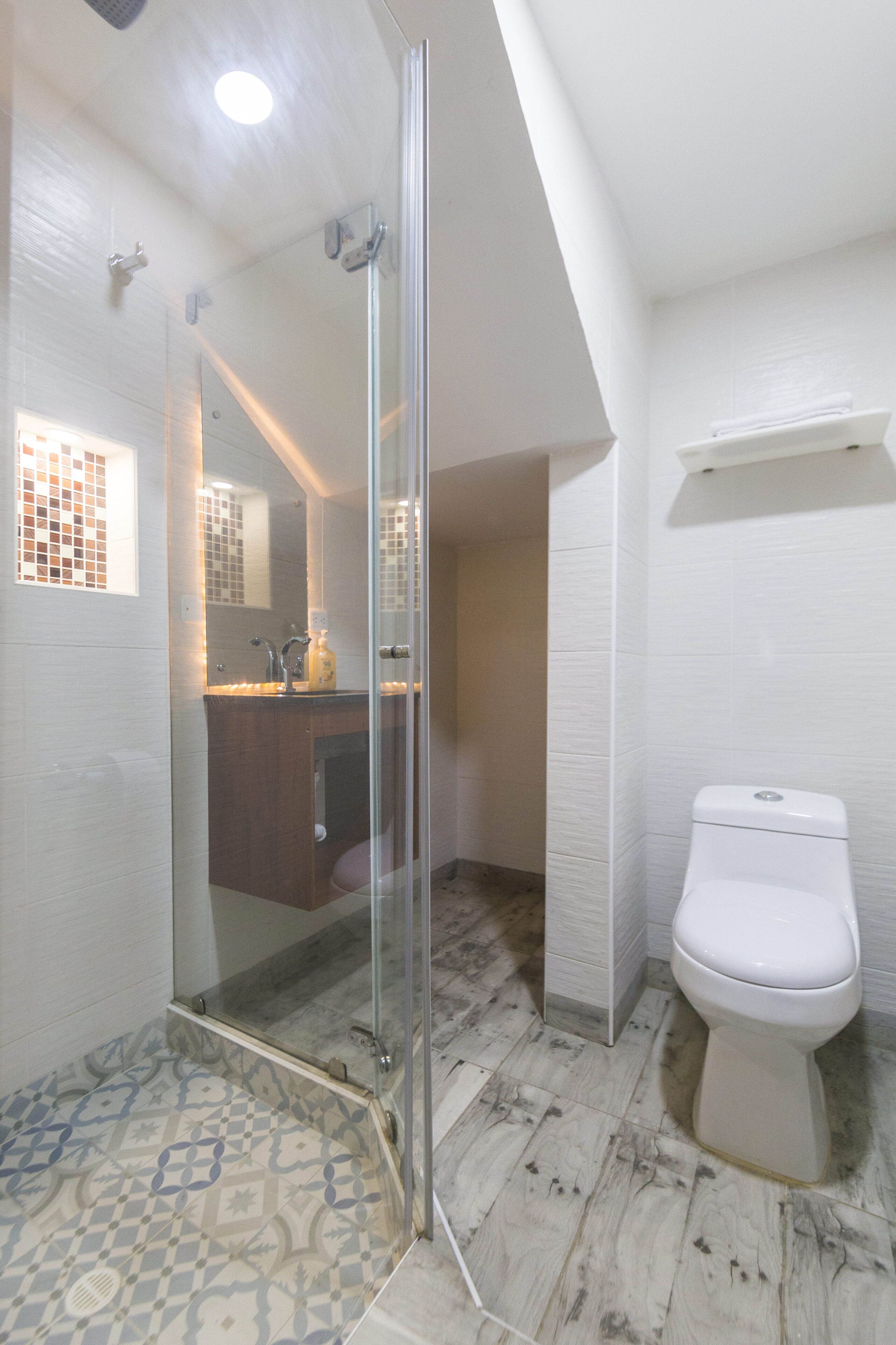 A bathroom with a glass shower enclosure, a white toilet, and patterned floor tiles.