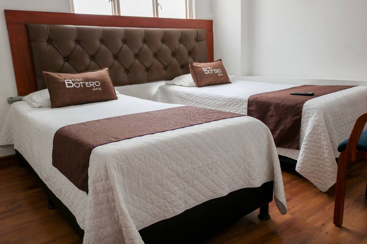 Two beds with brown headboards and pillows, a wooden floor, and a window in the background.