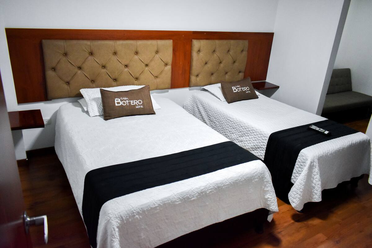 A hotel room with two beds, each with a headboard and pillows labeled "Botero Hotel".
