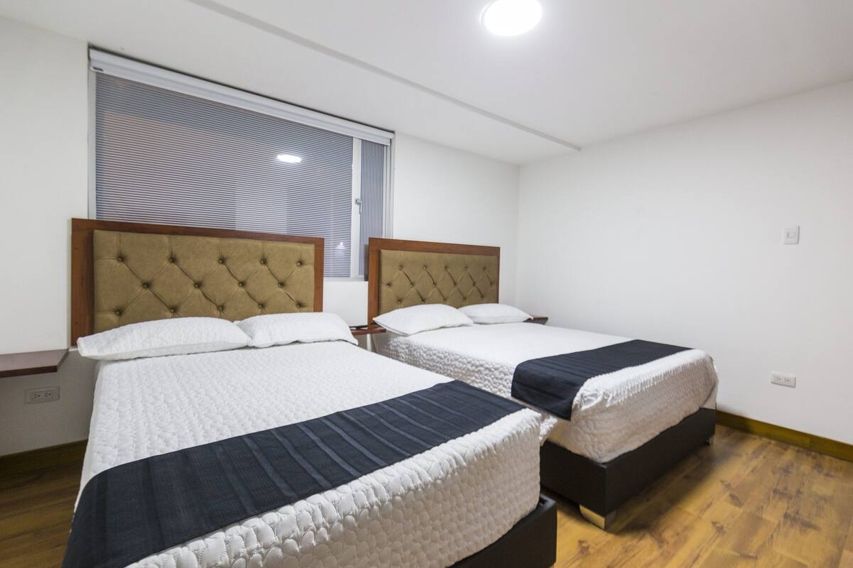 A hotel room with two beds, a window with blinds, and a wooden floor.
