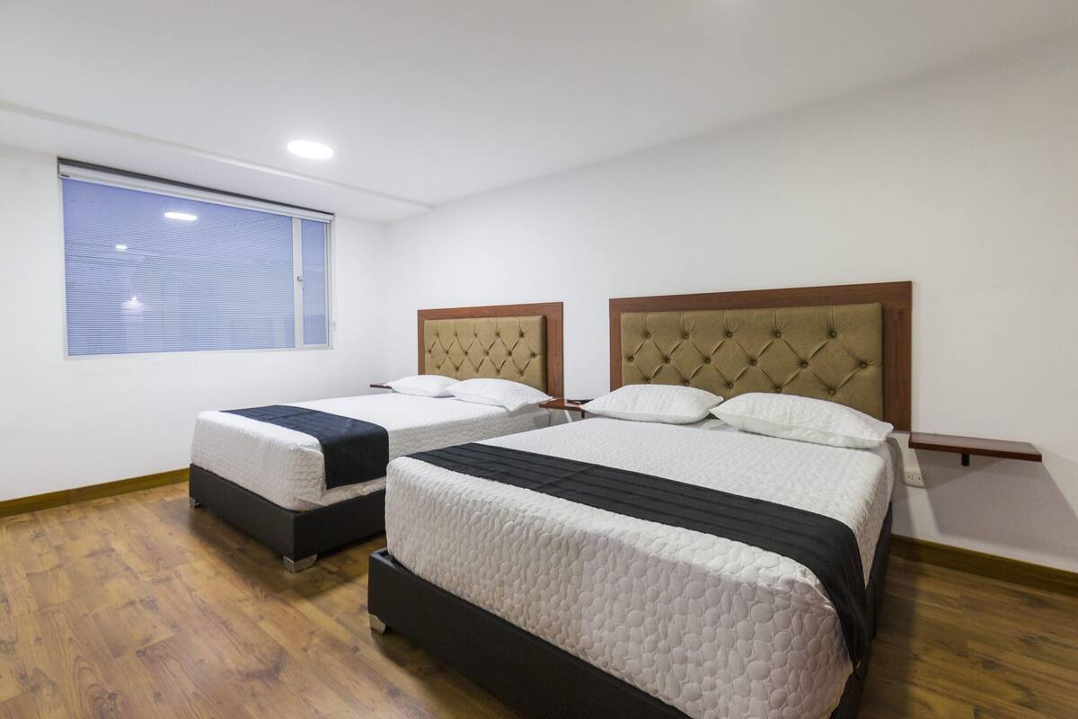 A room with two beds, a window, and a wooden floor.
