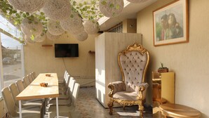 Un comedor con una mesa larga y sillas, un sillón capitoné, un televisor y luces decorativas colgantes.