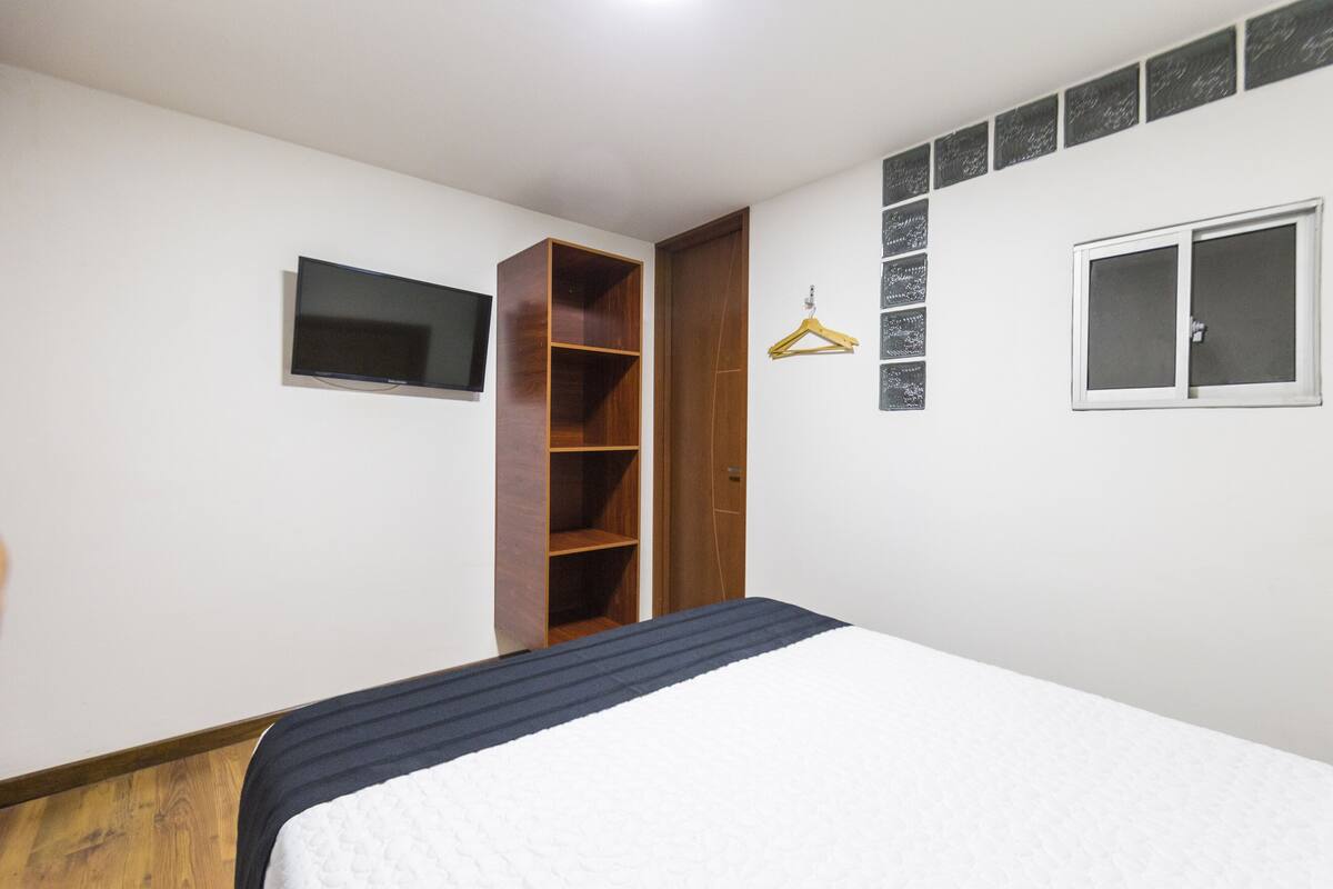 A bedroom with a bed, a wardrobe, a TV, a window, and a wall-mounted coat hanger.