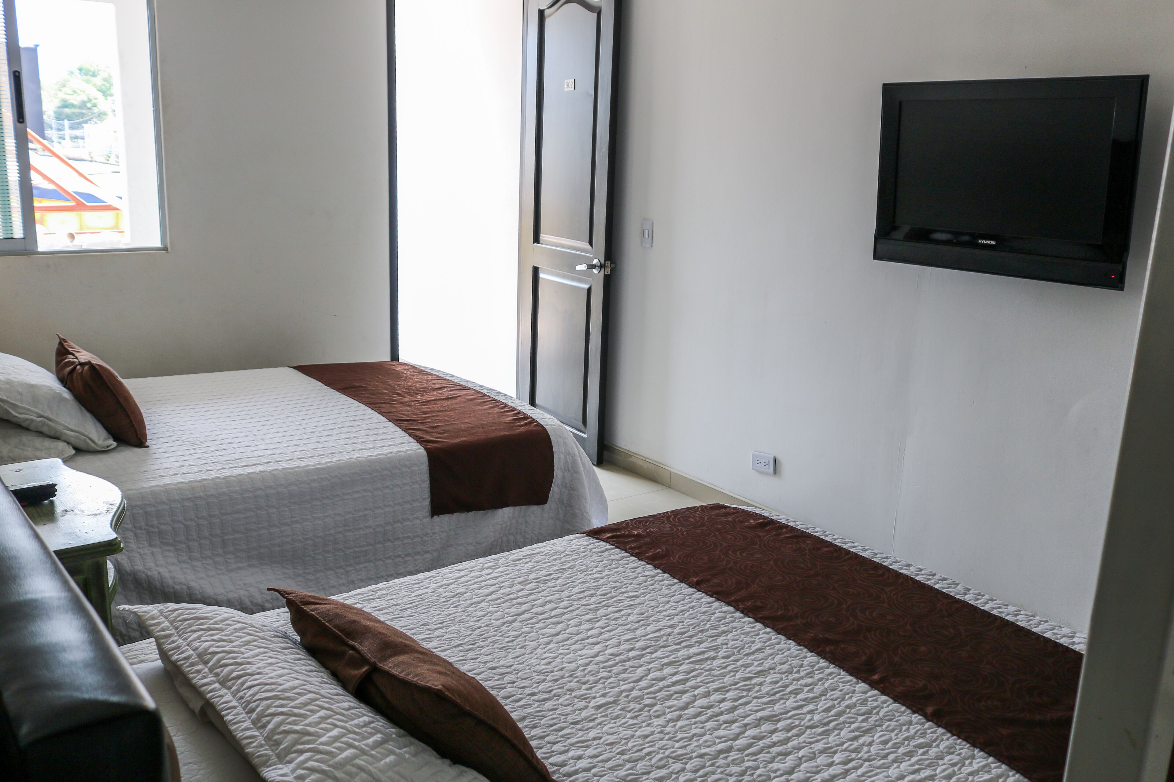 Una habitación con dos camas, un televisor montado en la pared y una ventana con persianas.