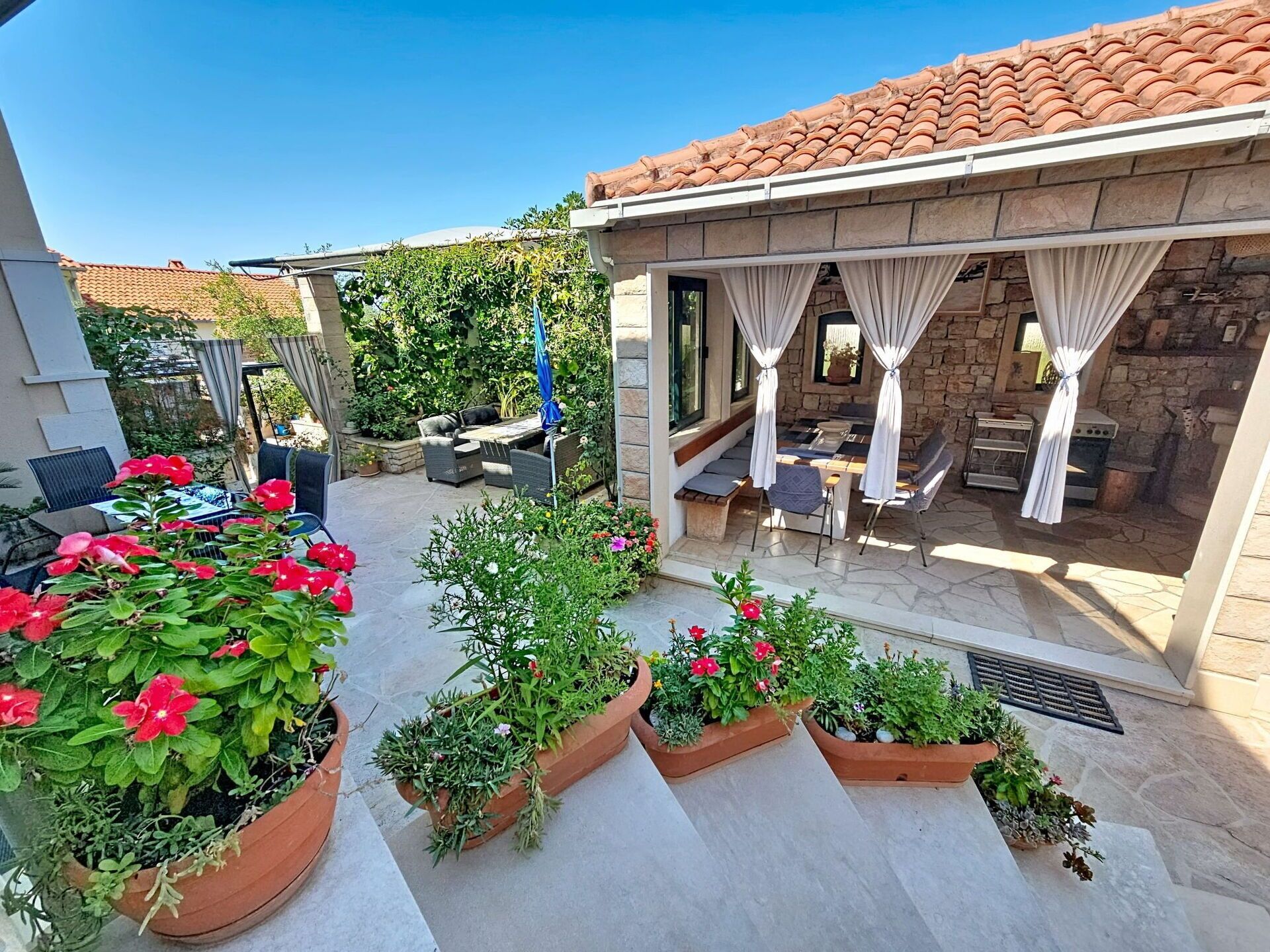 Un patio extérieur couvert, doté d’un sol en pierre, de plantes en pot et de mobilier d’extérieur.