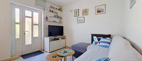 A living room with a sofa, a television, a small table, and a door leading to another room.