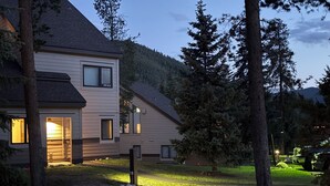 A modern two-story house with a well-lit entrance and a grassy yard. - Ski Keystone, Spacious Ground Floor Condo with Meadow Views &  Resort Amenities! (Keystone)
