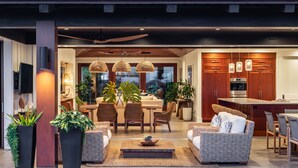 Ein modernes Wohnzimmer mit Essbereich, ausgestattet mit Korbmöbeln, einem Deckenventilator und einer Küche mit Holzschränken und Edelstahlgeräten.