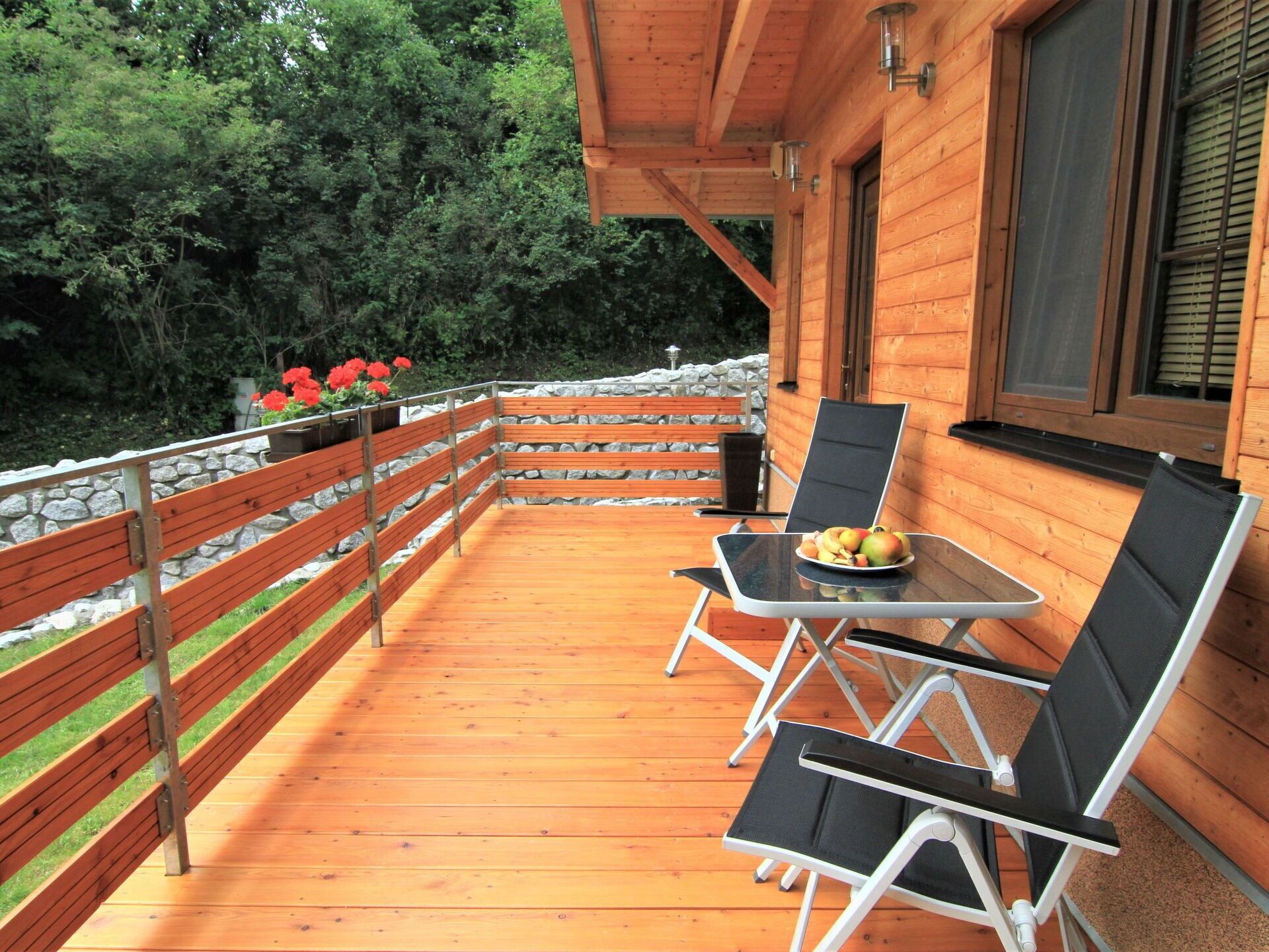Une terrasse en bois avec une table et des chaises, entourée d’un mur de pierres et de verdure.