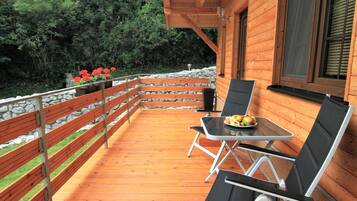 Une terrasse en bois avec une table et des chaises, entourée d’un mur de pierres et de verdure.