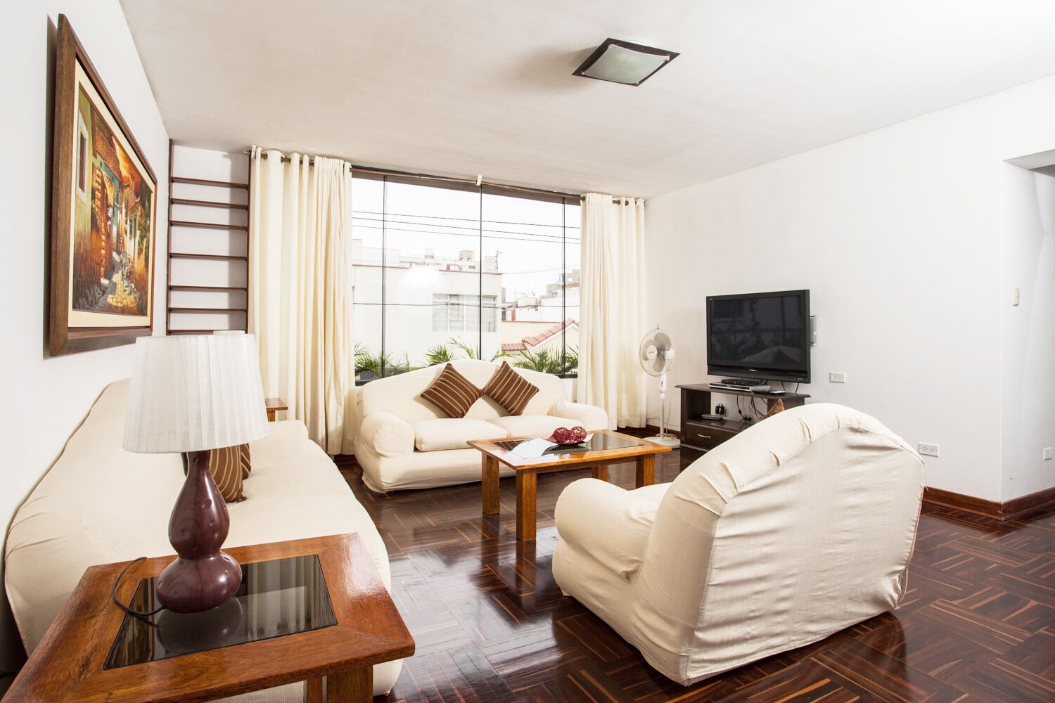 A living room with a sofa, armchair, coffee table, TV, and a painting on the wall.