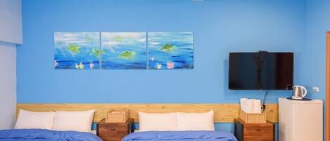Quarto com duas camas, televisão de tela plana, pequeno frigorífico e obras de arte na parede.