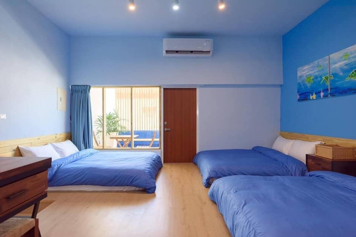 Une chambre avec deux lits, un bureau en bois, une fenêtre donnant sur un paysage agréable et un appareil de climatisation.