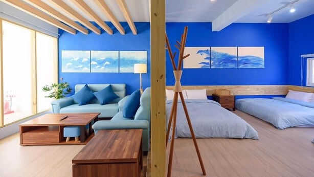 A modern room with a blue accent wall, a wooden ceiling, a sofa, a bed, and a painting. - Summer Homestay (Magong)