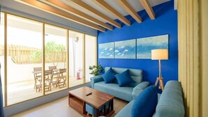 A modern living room with a blue accent wall, a sofa, a coffee table, and a large window with a view of the outdoors. - Summer Homestay (Magong)