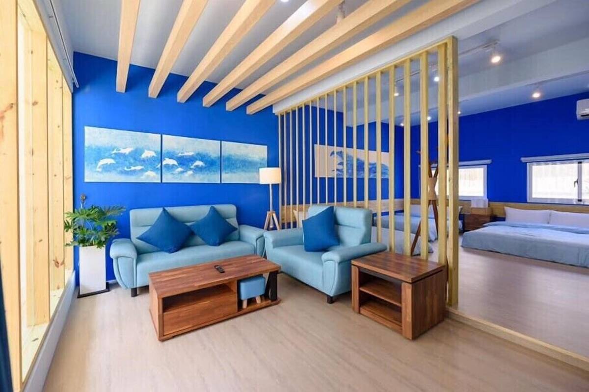 Un salon moderne avec un mur bleu, des poutres en bois au plafond, un ensemble de canapés et une table basse.