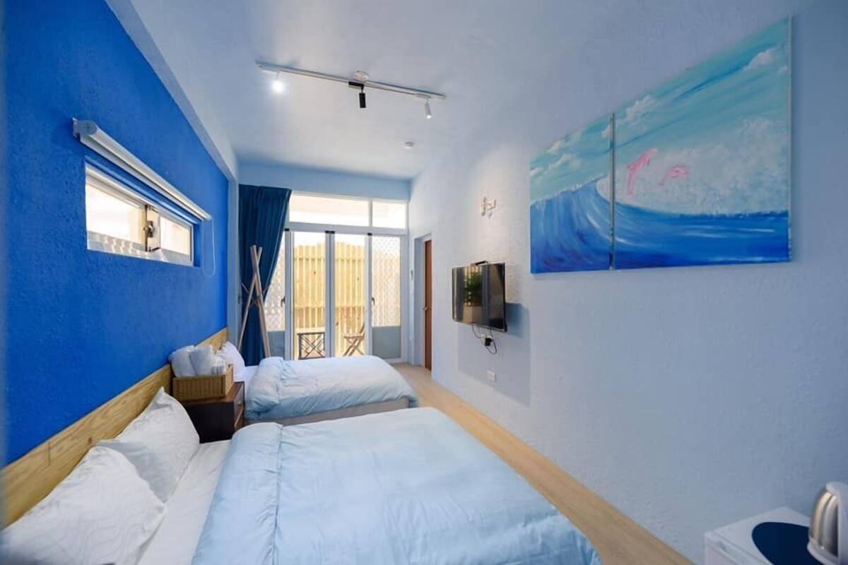 Une chambre d’hôtel avec deux lits, une télévision, un tableau représentant l’océan et une fenêtre donnant sur l’extérieur.