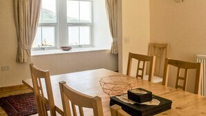 Un coin repas comprenant une table, des chaises, une fenêtre avec des rideaux et un luminaire fixé au mur.