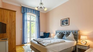 A bedroom with a large bed, a television, a wooden wardrobe, and a window with curtains.