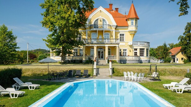 A large, yellow building with a red roof, a swimming pool, and outdoor seating.