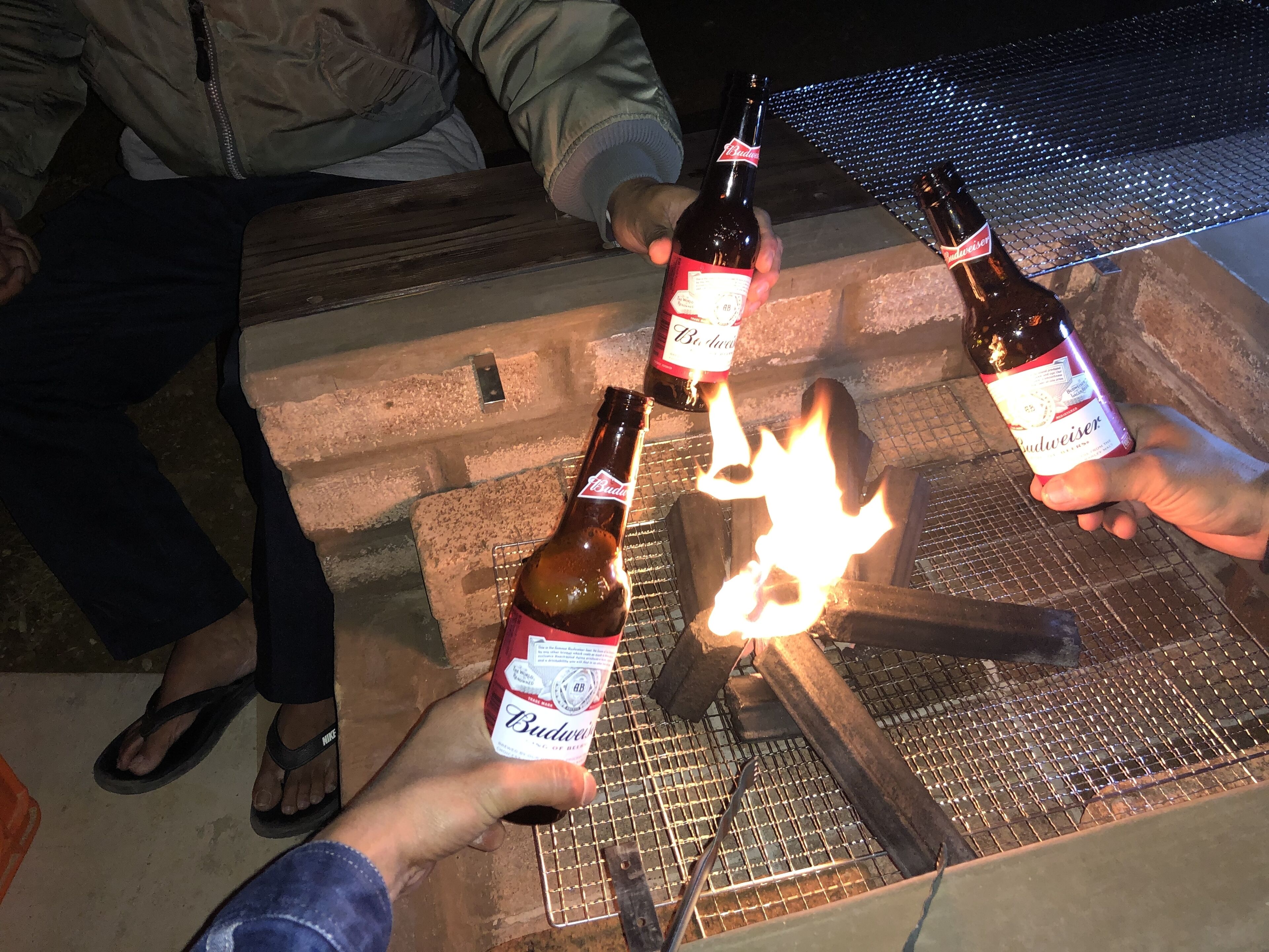 A person holding a Budweiser bottle with a lit match.