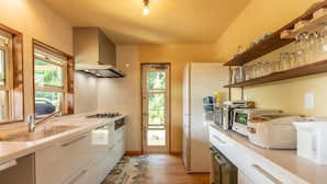 Una cocina moderna con armarios blancos, una estufa de acero inoxidable, horno empotrado, microondas y refrigerador. Hay un estante de madera sobre la encimera con cristalería.